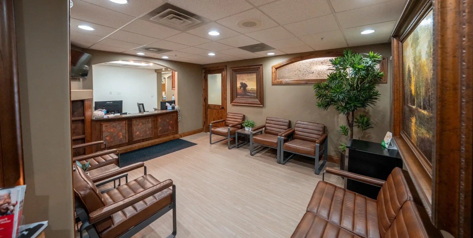 Dental office waiting area with brown leather chairs, framed wall art, and a wooden reception desk.